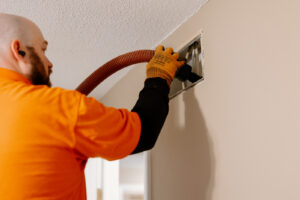 Technician cleaning a residential air duct vent with professional duct cleaning equipment.