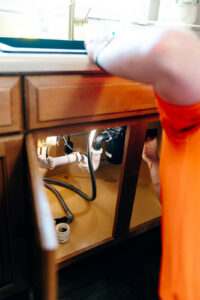 Summers PHC plumber working under a kitchen sink on the drain lines and P-trap during a drain cleaning service in Kokomo, Indiana