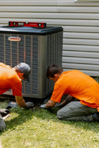 Two Summers PHC technicians installing and leveling a new Lennox AC condenser unit at a Kokomo, Indiana home
