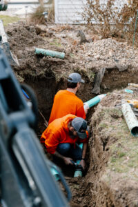 Professional plumbers installing underground sewer pipes in an excavated trench during a residential plumbing installation project.